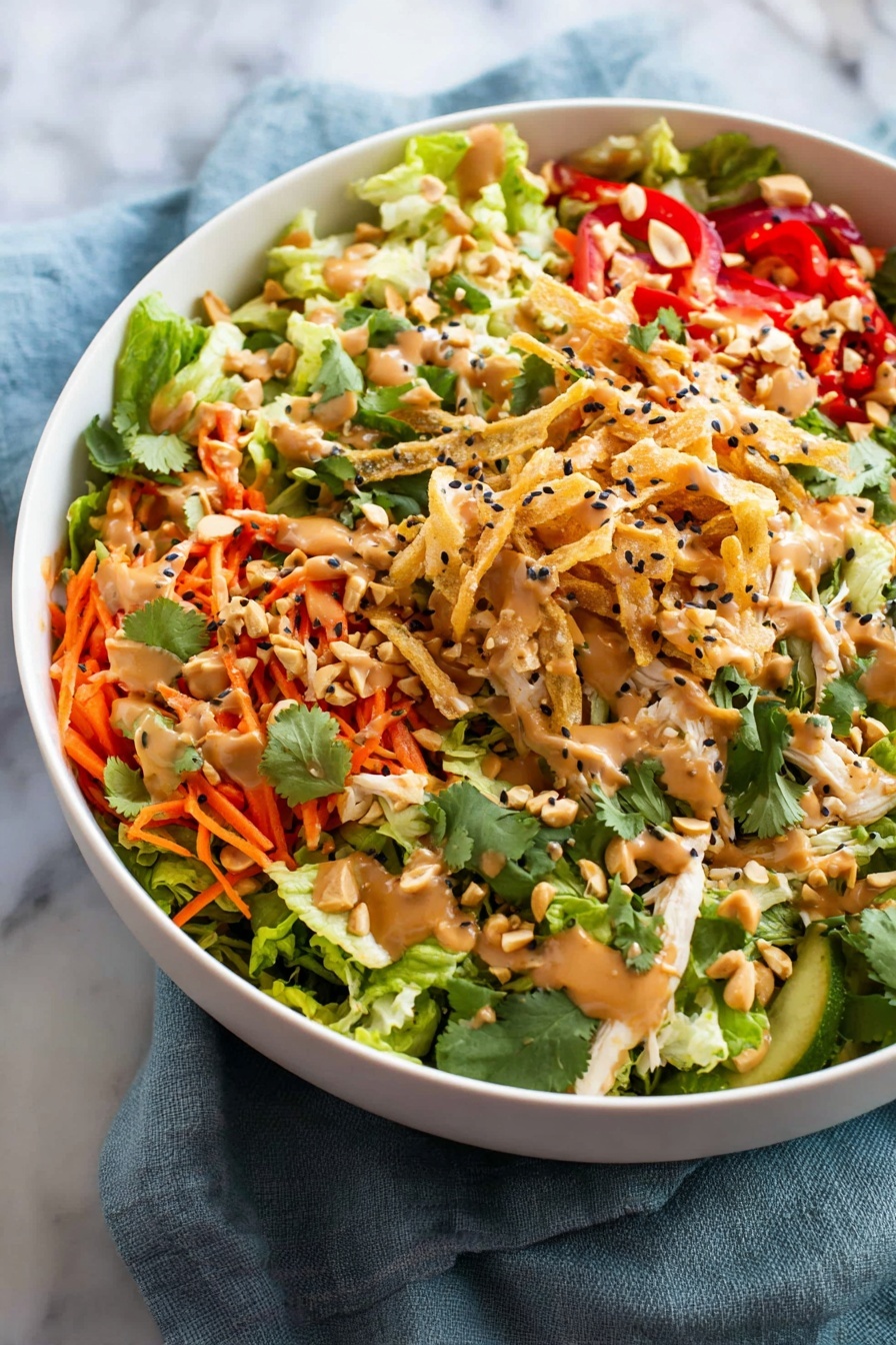 A large white bowl filled with a colorful salad that has four main layers: at the bottom is a bed of green leafy lettuce with light green and darker green leaves, on top of that are thin orange carrot strips and bright red bell pepper slices scattered evenly. The third layer has shredded light beige chicken pieces spread around, mixed with chopped peanuts and fresh green cilantro leaves. The top layer is drizzled with a creamy light brown dressing and sprinkled with black sesame seeds and crispy golden fried strips. The bowl sits on a soft blue cloth over a white marbled surface. Photo taken with an iphone --ar 2:3 --v 7
